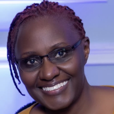 A person with dark skin, glasses, and a yellow shirt smiles at the camera. 