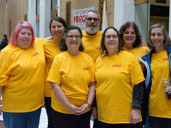 Group of Advocates staff members at the Caring Force Rally wearing their gold Caring Force t-shirts