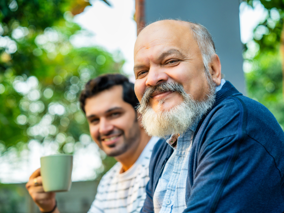 two male-presenting adults sitting on a porch smiling at the camera