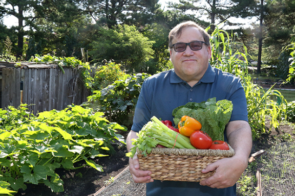 A light-skinned adult holds a basket of farm fresh veggies.