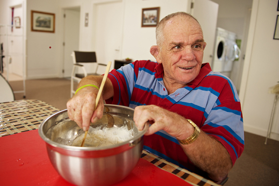 Older man in kitchen mixing ingredients in a bowl.
