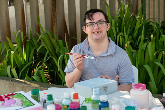 Young man with down syndrome smiling while working on a painting project.