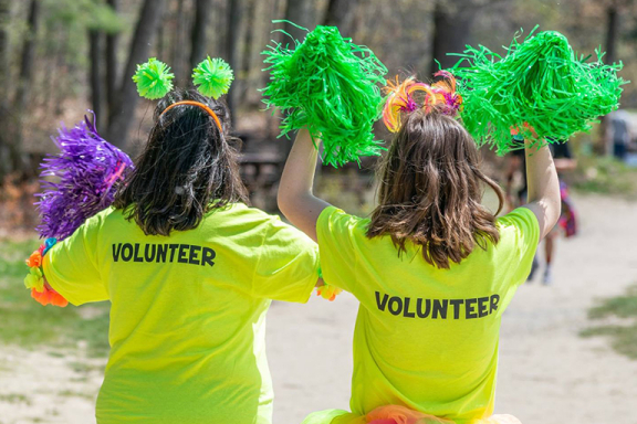 Back view of two people wearing volunteer shirts outside on a sunny day