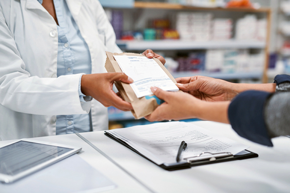 Closeup of pharmacist handing medication package to customer