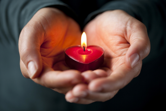 Hands holding a heart candle that is lit