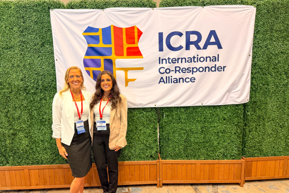 Two smiling adults standing in front of a banner for the International Co-Responder Alliance (ICRA)