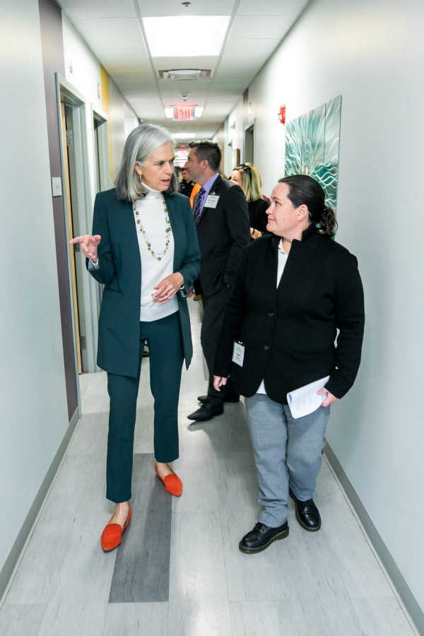Congresswoman Clark speaks with a woman in a dark jacket as they walk down a corridor