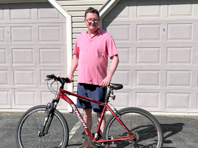 Jack, a young man, standing in front of his garage with his bike. He is wearing a pink polo shirt and has glasses.
