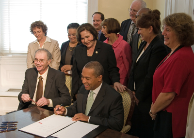 Bill Taylor, Governor Deval Patrick, and other elected officials gathered around a table as Patrick signs Chapter 257 bill.