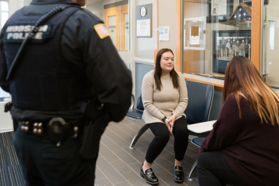 Person with brown hair speaking with a clinicians with a police officer watching