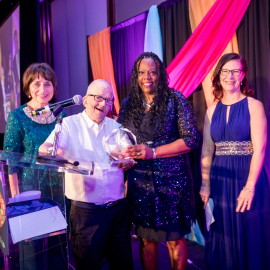 Five smiling adults on gala stage. Michael and Regina hold an award statue.