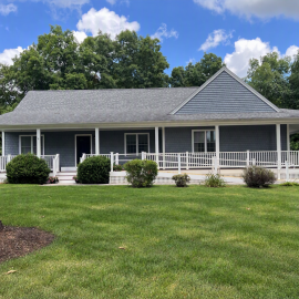 A large new home with a sprawling lawn and wraparound front porch