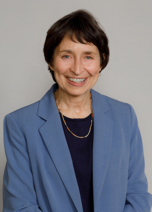 An adult with short dark hair and a blue blazer smiles in a professional headshot